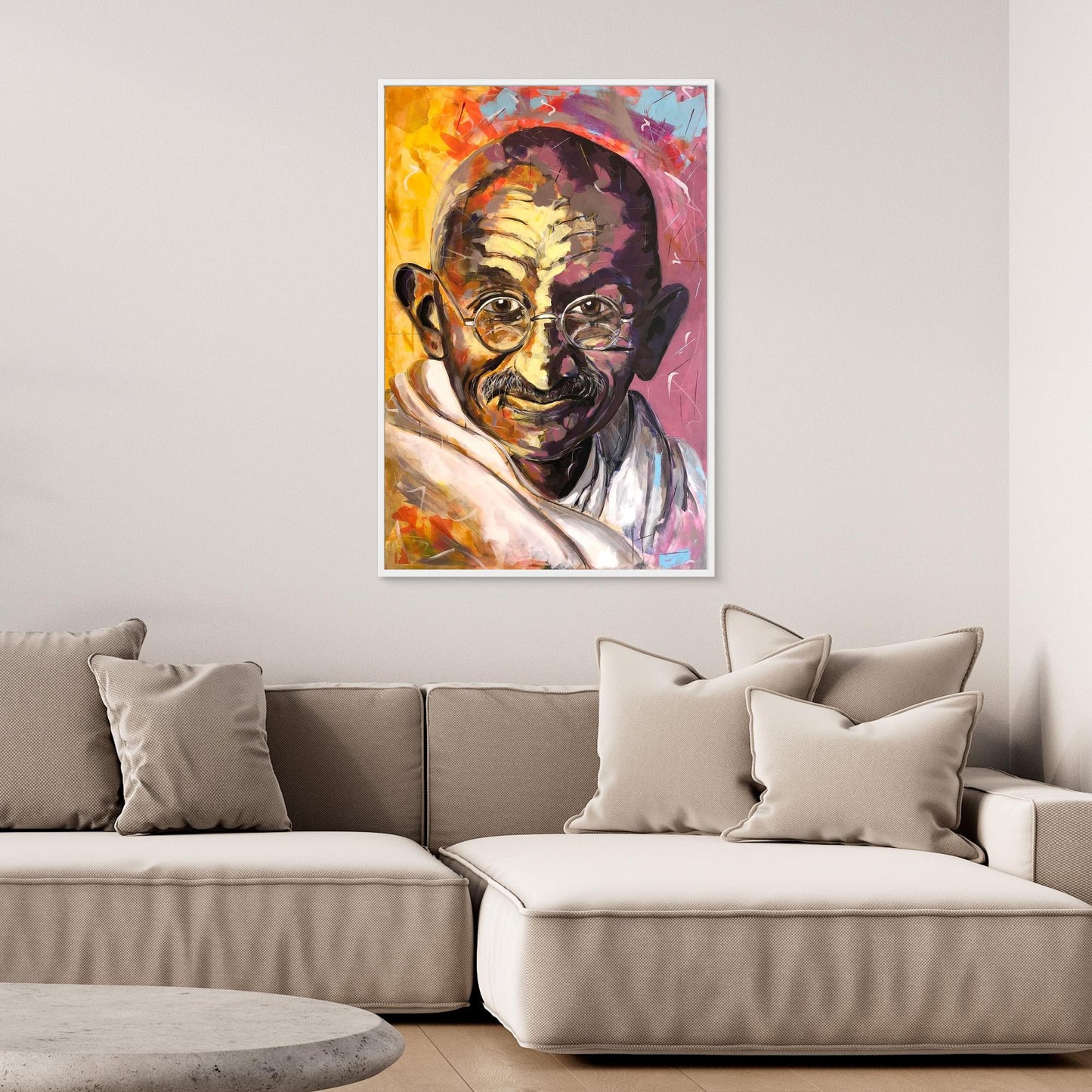 A canvas print of Gandhi displayed above a modern, comfortable beige sofa with cushions, in a room setting.